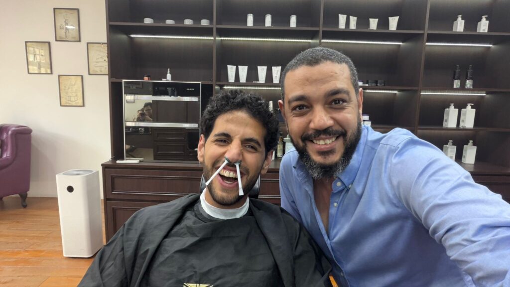 Nas Daily (Nuseir Yassin) enjoying a fun nose waxing session at The British Barbers in Singapore's Chinatown. He's smiling with cotton sticks in his nose while posing with the barber – clean, precise, and surprisingly comfortable facial grooming!